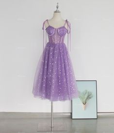 a purple dress on display in front of a white wall with a framed photo next to it