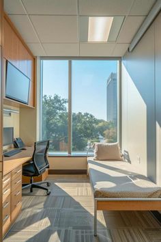 an empty room with a bed, desk and large window overlooking the trees outside it