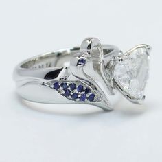 a white gold ring with blue sapphires on the sides and a heart shaped diamond in the middle