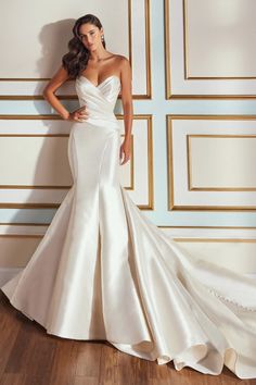 a woman in a white wedding dress leaning against a wall with her hands on her hips