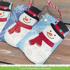 three snowmen with hats and scarfs hanging from strings on a wooden table top