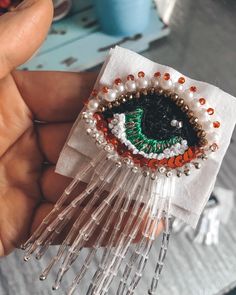 someone is holding up a beaded brooch that looks like an eye with beads on it