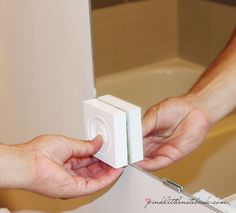 two hands are holding an electronic device in front of a mirror that is on the wall