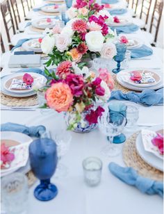 a long table is set with blue and white plates, napkins, and flowers