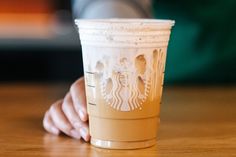 a person holding a starbucks cup on top of a wooden table