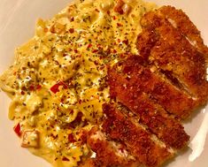 two pieces of meat and macaroni on a white plate with red pepper sprinkles