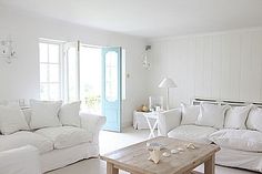 a living room filled with white furniture next to a blue door and window sill