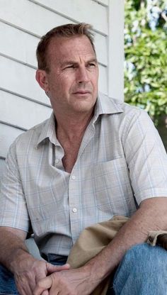 a man sitting on the porch in front of a house with his hand on his knees