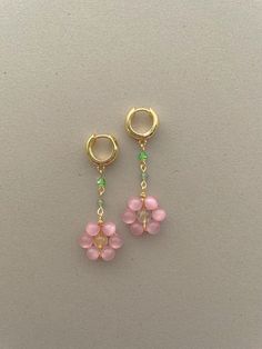 two small pink flowers hanging from gold hoop earrings on a white surface with green beads