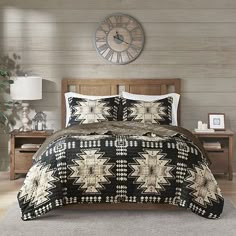 a bed with a black and white comforter on top of it next to a wooden dresser