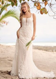 a woman in a wedding dress standing on the beach under a tree with her bouquet