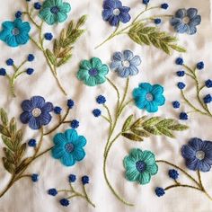 blue and green flowers are embroidered onto a white linen material with stitching on it