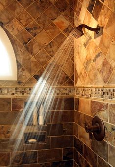 a shower head with water coming out of it in a tiled wall next to a window