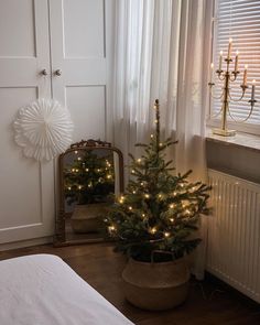 a small christmas tree sitting next to a window in a room with white curtains and lights on the windowsill