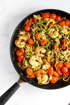 a skillet filled with pasta, shrimp and tomatoes on a white counter top next to a spatula