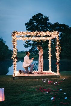 a man kneeling down next to a woman in front of a lit up gazebo