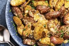 a blue bowl filled with potatoes covered in seasoning and garnished with parsley