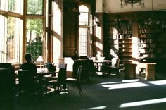 the sun shines through large windows into a library with bookshelves and tables