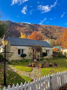 a white picket fence in front of a house with fall foliage on the mountain behind it