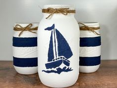 three painted mason jars sitting on top of a wooden table with rope tied around them