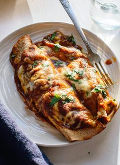 a white plate topped with meat covered in sauce and cheese next to a glass of water