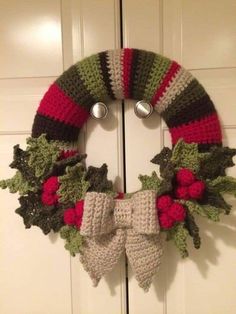 a crocheted christmas wreath hanging on the front door with holly leaves and bells