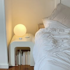 a white bed sitting next to a night stand with a lamp on top of it