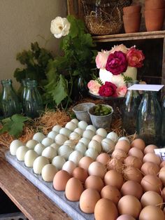 an assortment of eggs and flowers on display in front of a table with vases