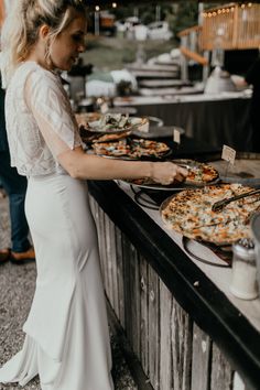 a woman in a white dress standing next to a table with pizzas on it