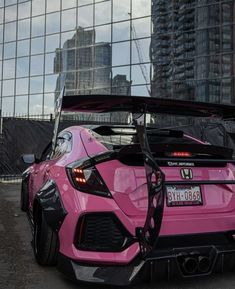 a pink sports car parked in front of a tall building with its hood up open