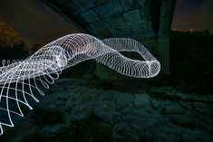 a long exposure photo of a light sculpture in front of a stone bridge at night