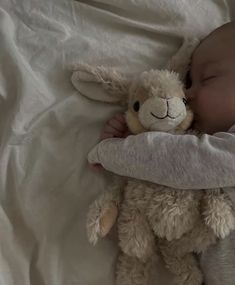 a baby sleeping with a stuffed animal on it's back in a bed next to a white sheet