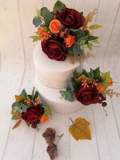 a three tiered wedding cake with flowers and leaves on the top, sitting on a white table