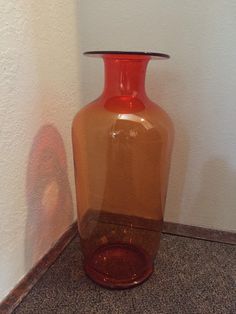 a red vase sitting on the floor next to a wall