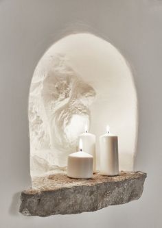 two white candles sitting on top of a stone shelf in front of a cave window