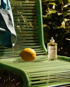 an orange sitting on top of a green bench next to a bottle of cologneine