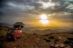 a red van parked on top of a lush green hillside under a sky filled with clouds