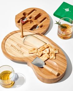 two wooden cutting boards with cheese, crackers and a knife on them next to some glasses