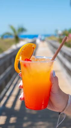 a hand holding a drink with an orange slice on the rim and a straw in it