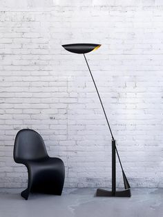 a black chair sitting next to a lamp on top of a table in front of a white brick wall