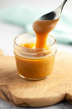 a spoon full of orange sauce sitting on top of a wooden cutting board