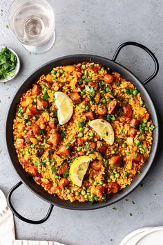 a skillet filled with rice, peas and lemons on top of a table