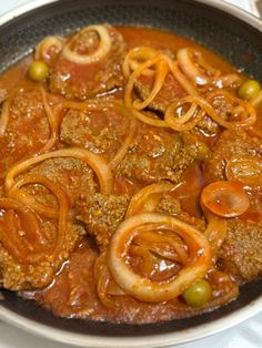 meat with onions and olives in a pan on the stove top, ready to be cooked