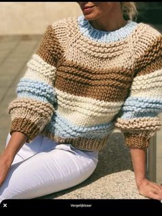 a woman sitting on the steps wearing white jeans and a sweater with multicolored stripes