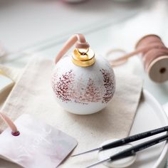 a white vase sitting on top of a table next to some scissors and thread in front of it