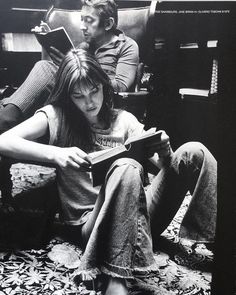 a black and white photo of two people sitting on the floor, one reading a book