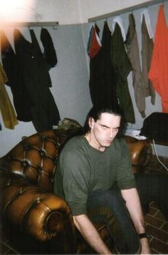 a man sitting on top of a brown couch in front of a bunch of clothes