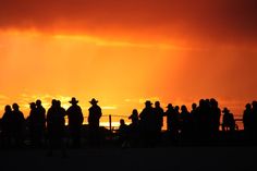 a group of people standing on top of a sandy beach under a cloudy orange sky