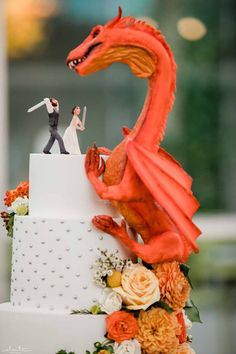 a wedding cake with a red dragon figurine on top and an orange flower arrangement