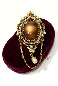 "Vintage Originals By Robert brooch pendant is sensational. Handmade in gold plated molded metal it features a large oval topaz marbled glass center stone mounted in a fancy crown prong setting. A lovely French flier de lis sits at the top with faux pearl and small domed topaz glass cabochon accents. A pearl with a ridged fluted cap dangles at the bottom, the bar link chain swag is a fabulous finishing touch! Even the back has framed carved flower bouquet and hook for wearing as a pendant. Signed Original By Robert on a metal cartouche.  Original By Robert jewelry is not easily found and has become increasingly more desirable and collectible. Very high quality materials and fine workmanship goes into each hand made piece. The brooch is in excellent condition ... I've never seen another one Fancy Crown, Victorian Revival, Antique Brooches, Gold Tone Metal, Metal Chain, Vintage Signs, Tiger Eye, Link Chain, Prong Setting